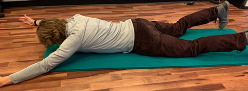 Man lying face down on an exercise mat with arms stretched out in front of his body