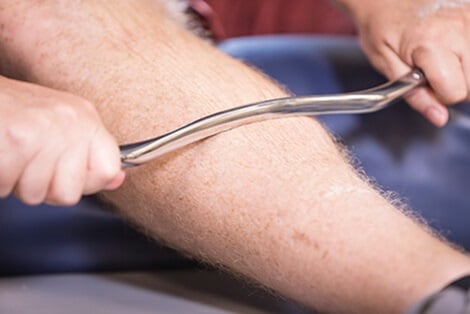 Hands grasping sculpted metal rod and pulling upward on man's leg.