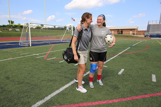 Female soccer player standing on the field with her trainer.