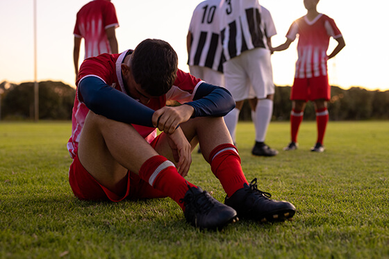 Injured male soccer player sitting on the field with his head down.