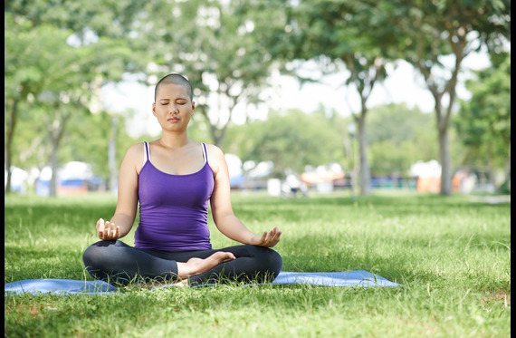 A cancer patient sitting in a park on a blanket doing yoga exercises.