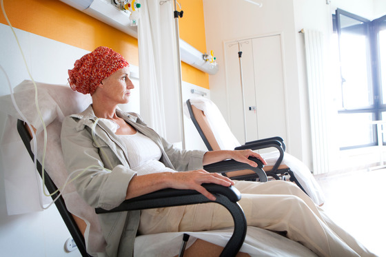 A female cancer patient sitting in a chair receiving chemo treatment through an IV. 