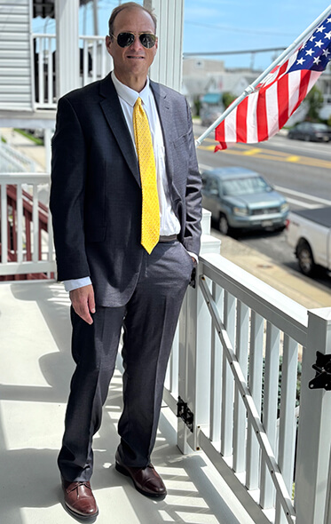 Photo of Kevin in a suit in front of an American flag